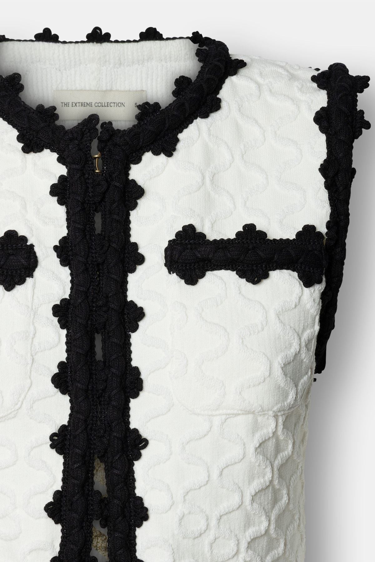 Chaleco de lujo blanco para mujer modelo Tristan con perfiles festoneados en negro.
